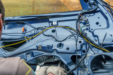 Car repairman near the disassembled car door and fiddling with the wires from the alarm. The concept of repair of the wiring of car door