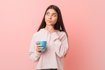 Young arab woman holding a cup looking sideways with doubtful and skeptical expression.