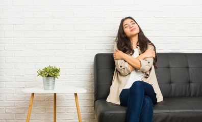 Young arab woman sitting on the sofa hugs, smiling carefree and happy.