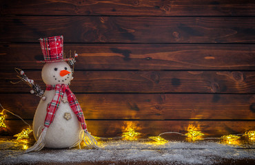 Christmas background with Christmas lights and snowman on the old wooden board
