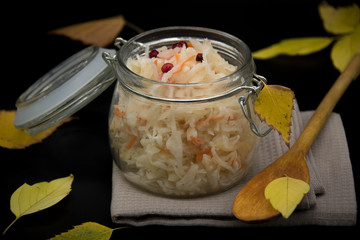 Sauerkraut in a glass jar on a black background with yellow leaves.