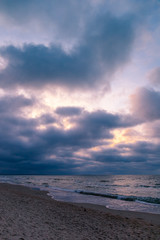 sandy beach by the sea with gloomy cloudy weather in the purple light of sunset