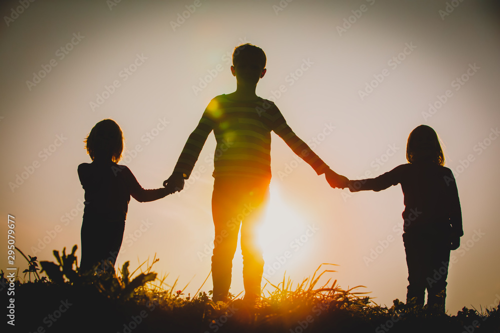 Wall mural silhouettes of kids - boy and girls - holding hands at sunset