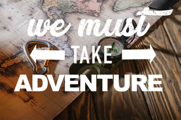 compass, safety hook and map on wooden table with we must take adventure illustration