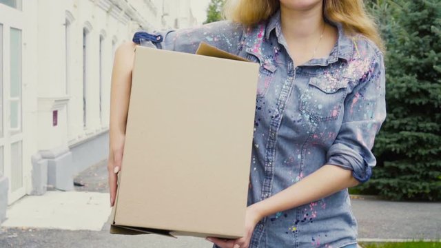 Young woman carrying a cardboard box and walking outdoor