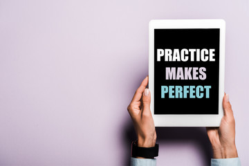 cropped view of woman holding digital tablet with practice makes perfect lettering on purple