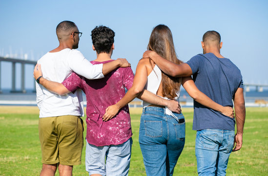 Team of friends embracing outside. Backs of young men and woman standing in line on grass, hugging each other. Friendship or unity concept