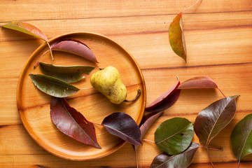 Pear, bright leaves, wooden plate on a wooden table