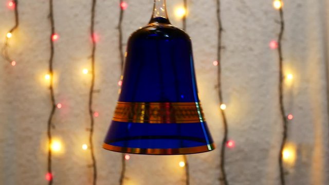 A blue glass bell sways against the background of Christmas lights. christmas and new year celebration concept