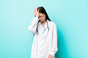 Young chinese doctor woman forgetting something, slapping forehead with palm and closing eyes.
