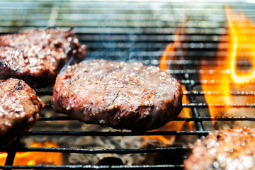 Burgers are cooking on grill with open flames