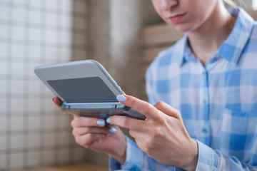 Close up view of woman hand using grey handheld game console at bright living room. Gaming, hobby, technology, entertainment, portable, video game and leisure time concept