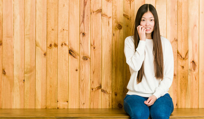 Young chinese woman sitting on a wooden place biting fingernails, nervous and very anxious.