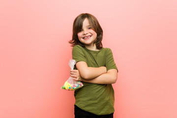 Little boy caucasian holding candies smiling confident with crossed arms.