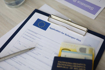 Modern wooden table with printed application for schengen visa, passport and money. Travelling...