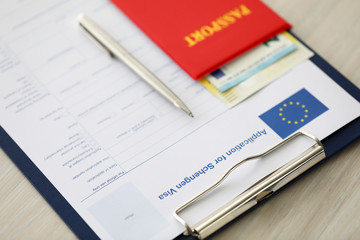Focus on document case with application for schengen visa, passport, money and pen lying on table in office. Filling questionnaire form. Travelling abroad or immigration concept. Blurred background