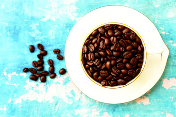 White cup of roasted coffee beans on blue background