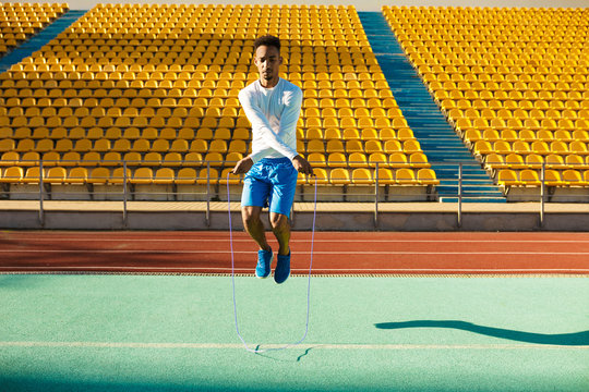 Young handsome African American sportsman jumping on skipping rope during workout at stadium
