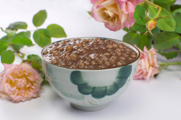 Brazilian dessert made of tapioca pearls called sagu in chocolate flavor in a bowl with roses in the background