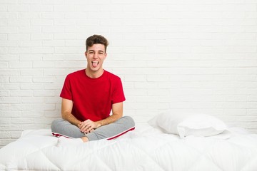 Young teenager student man on the bed funny and friendly sticking out tongue.