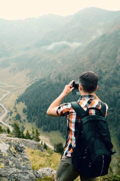 young man takes pictures on a cell phone and enjoying mountain landscape, the concept of hiking with lightweight modern gadgets for photographing travel and lifestyle, outdoor adventure