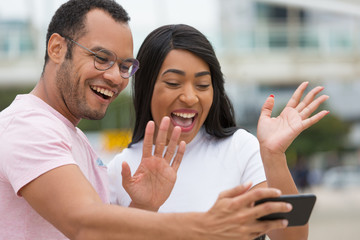 Happy young people smiling to camera. Smiling multiracial couple standing on street and waving to phone camera. Concept of self portrait