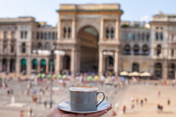 Lady’s hands holding a cup of cappuccino coffee at the view of Galleria Vittorio Emanuele at...