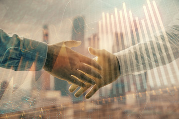 Naklejka na ściany i meble Double exposure of financial graph on cityscape background with two businessman handshake. Concept of stock market deal