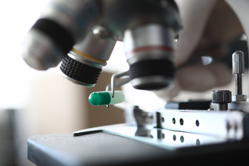 Focus on metallic tweezers holding drugs. Laboratory research of marijuana medicines under microscope. Medicine and healthcare concept. Blurred background