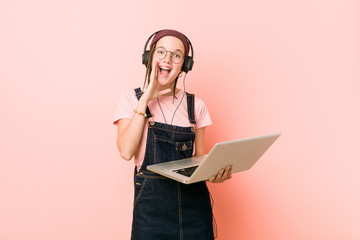 Young caucasian woman holding a laptop shouting excited to front.