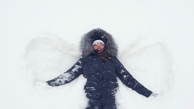 Happy girl lying on a snow and shows angel, slow motion