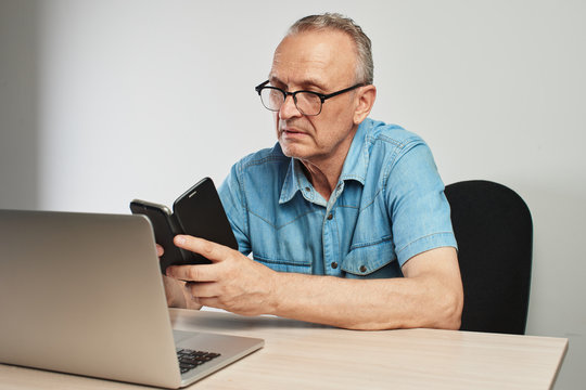 Elderly Caucasian man in glasses with a serious expression on his face working on a laptop at his desk on a white background
