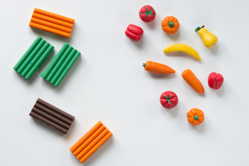 Pieces of polymer clay and handmade fruits and vegetables from it on white background