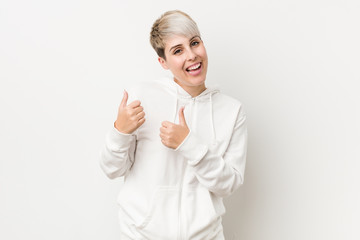 Young curvy woman wearing a white hoodie raising both thumbs up, smiling and confident.