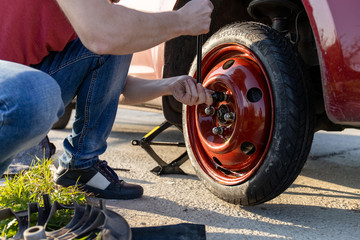 a man fastens a spare tire instead of a punctured one on the road