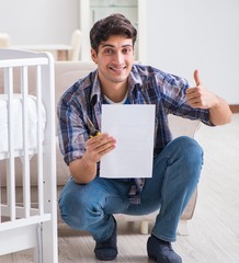 Young man assembling baby bed with instruction manual