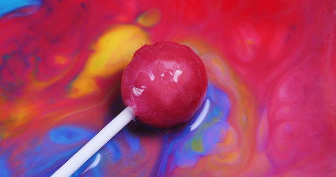 Macro shot of pink lollipop laying on colorful paint