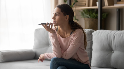 Young woman holding phone using mobile voice recognition at home