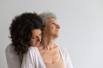 Peaceful pensive adult daughter hugging senior mother. Middle aged woman embracing elderly lady. Family relations concept