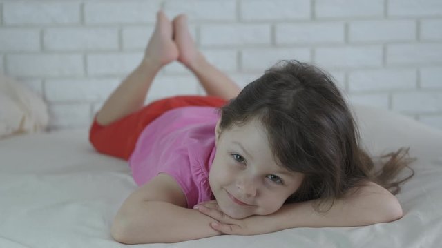Kid lay in the bed. Charming little girl lies in bed and looks at the camera.