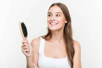 Young caucasian woman holding a hair brush smiling confident with crossed arms.