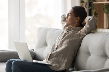 Happy dreamy woman relaxing stretching sit on couch with laptop