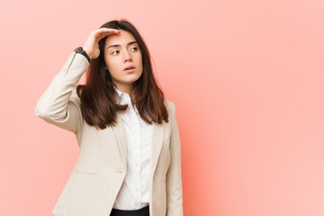 Young brunette business woman against a pink background looking far away keeping hand on forehead.