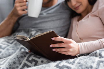Obraz premium cropped view of girlfriend reading book and boyfriend holding cup of tea