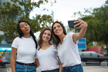 Front view of smiling women posing for selfie on street. Cheerful young ladies taking selfie with smartphone. Concept of self portrait