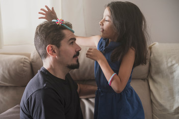 Father playing with daughter with diadem at home