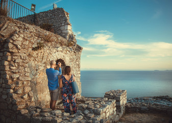 RAGAZZO E RAGAZZA TURISTI DI SPALLE CHE FOTOGRAFANO CON IL CELLULARE IL PANORAMA DEL MARE VISTO DA UN TEMPIO ANTICO IN ITALIA