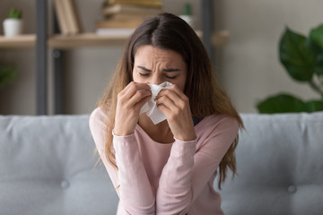 Allergic ill woman holding tissue blowing running nose