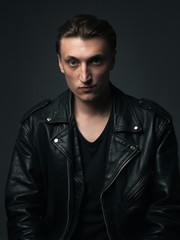 Portrait of young serious man in leather jacket in studio