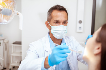 Fototapeta na wymiar Professional dentist wearing medical mask, examining teeth of a patient